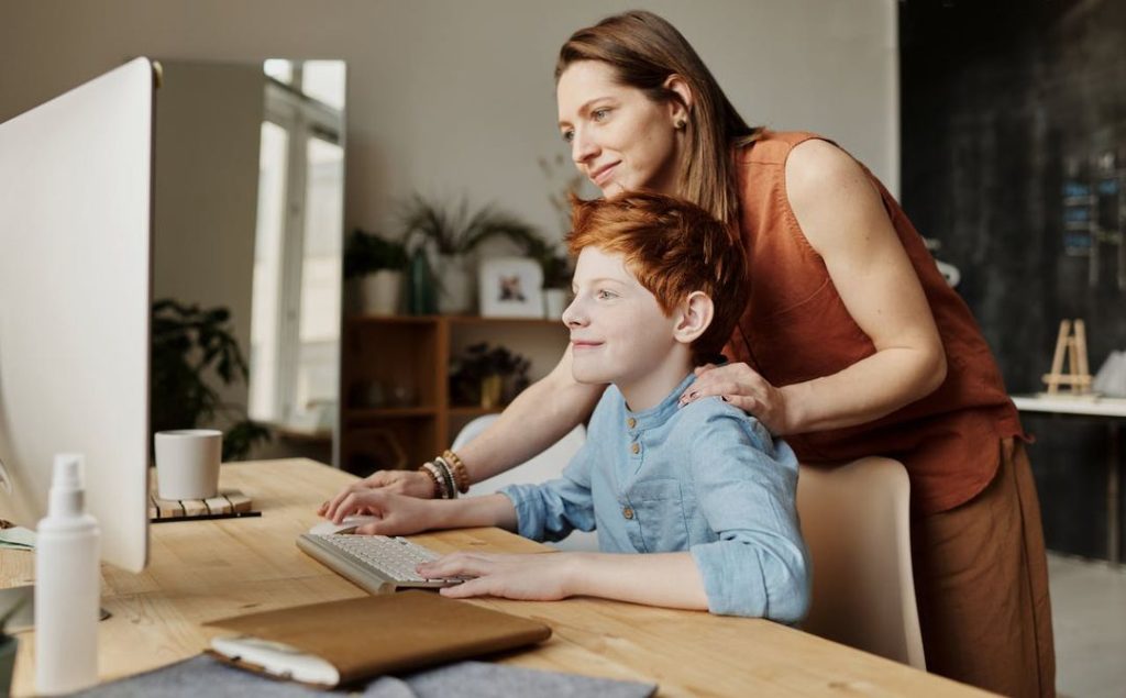 Photo Of Woman Tutoring Young Boy looking at a computer screen.