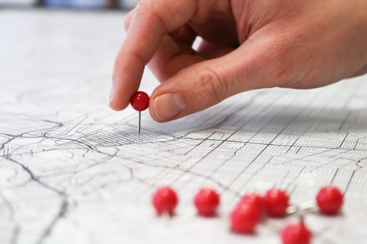 Closeup shot of a person's hand placing a pin on a city map.